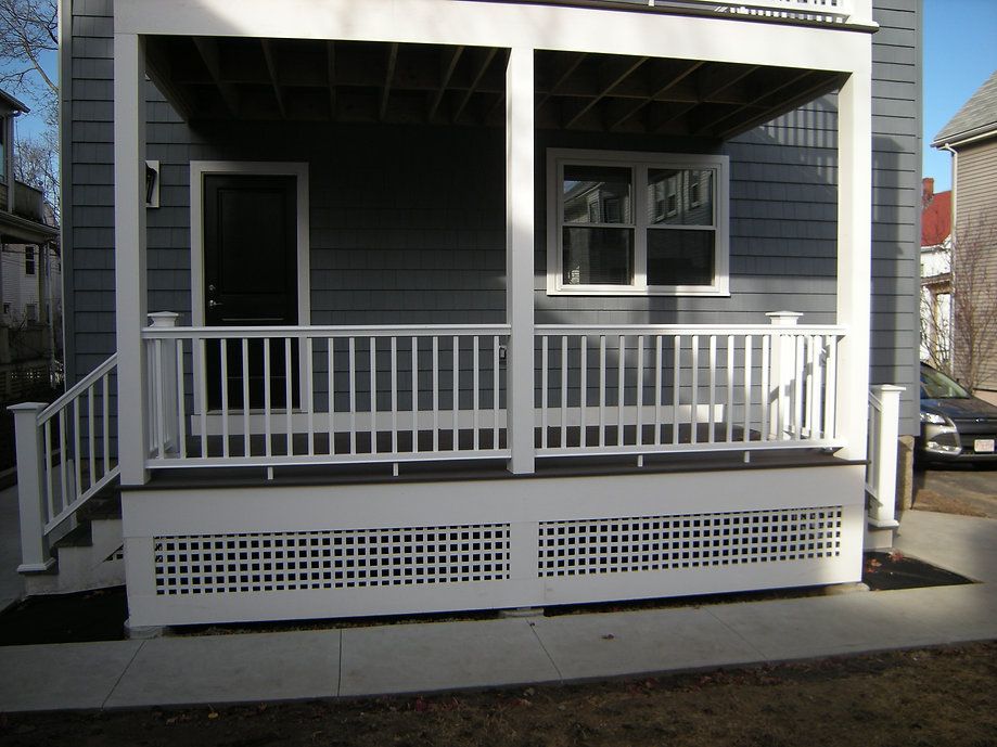 White deck with railing, lattice skirting, gray house, black door, window, and steps.