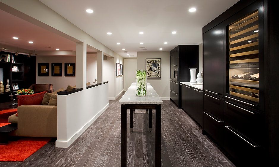 A modern basement with a wine fridge, bar, and seating area. Dark wood floors and black cabinetry.