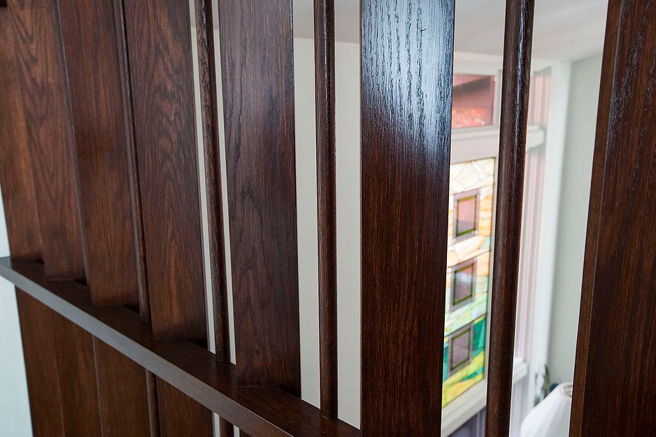 Dark wood staircase railing with vertical slats, view through to stained glass window.