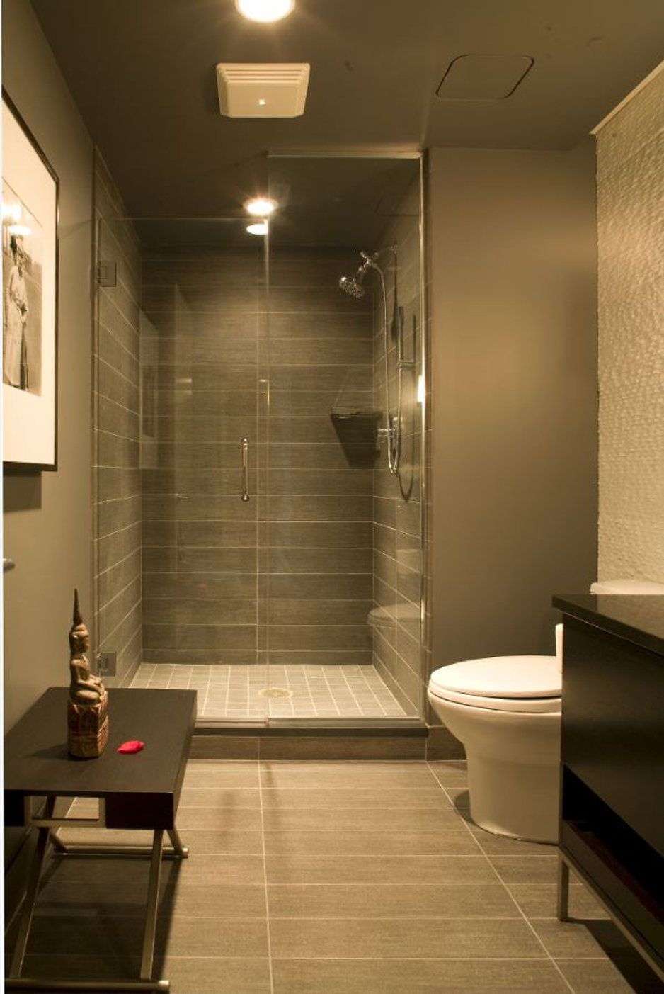 Modern gray bathroom with a glass shower, toilet, and small table.