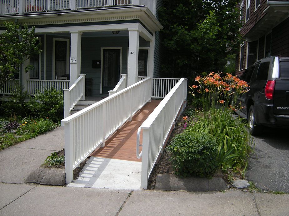 Ramp leading to a light green house's porch; white railings on both sides.