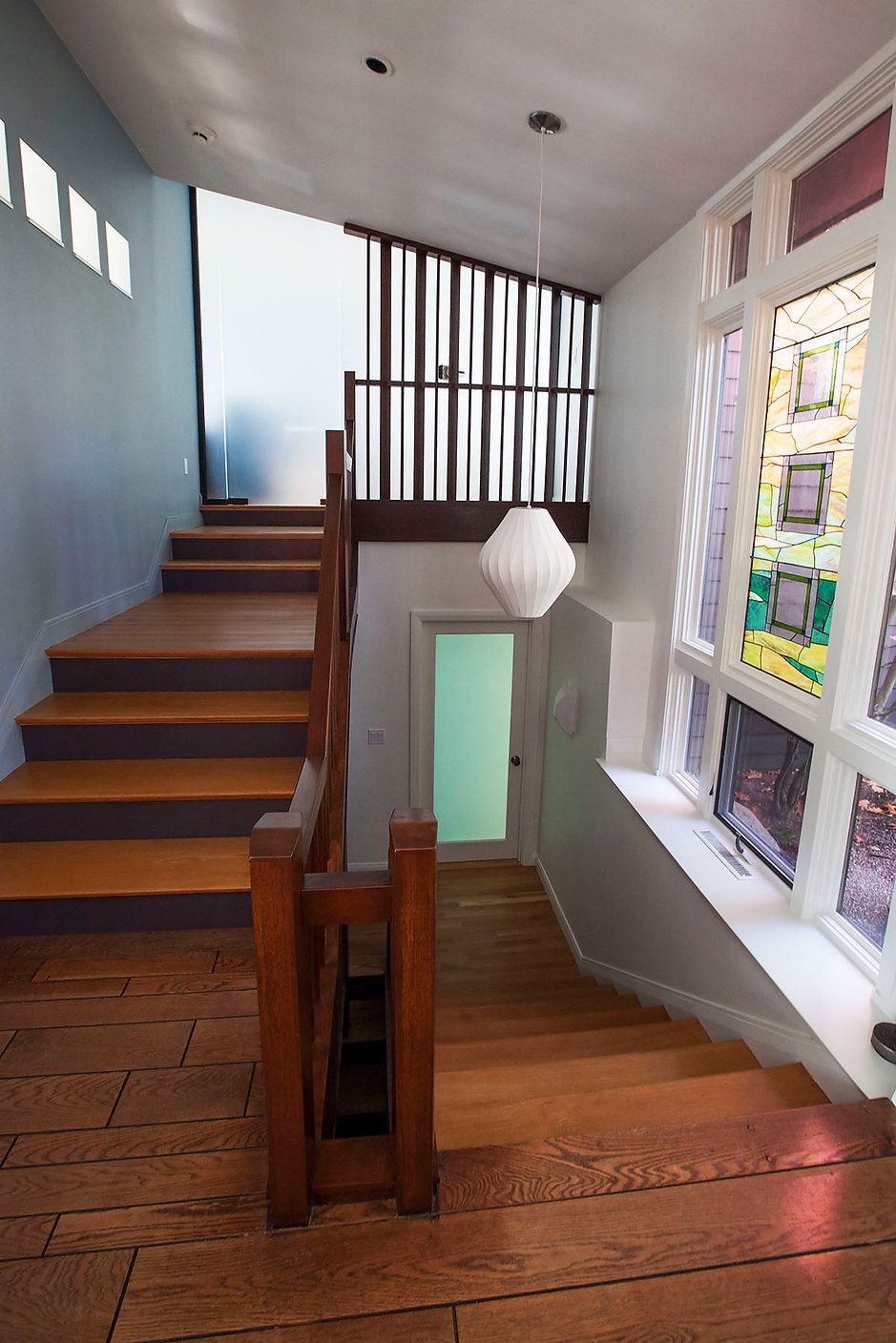 Wooden staircase in a home, with stained glass window. Brown wood flooring and banister.