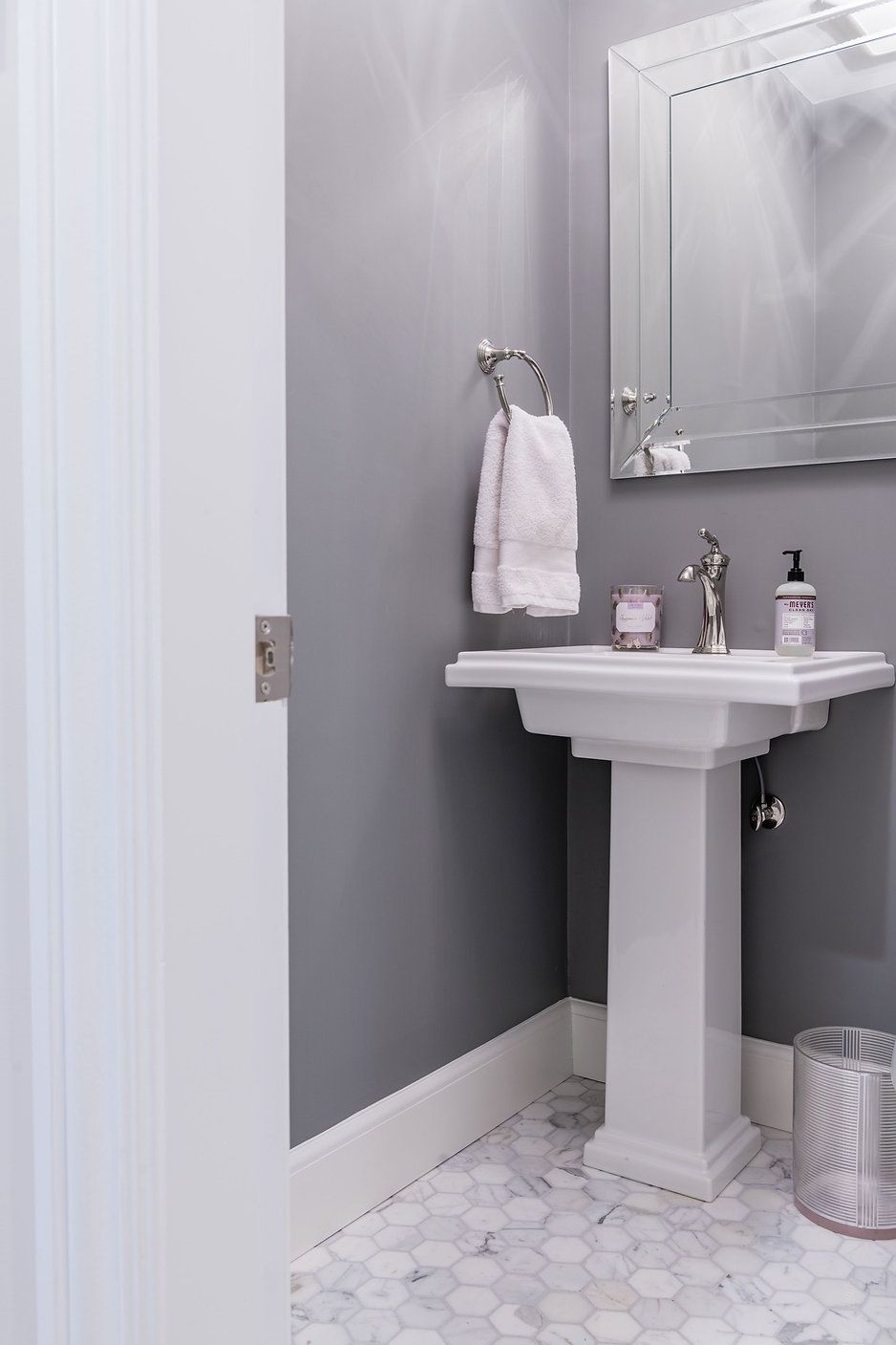 Gray powder room with white pedestal sink, mirror, and hexagon tile floor.