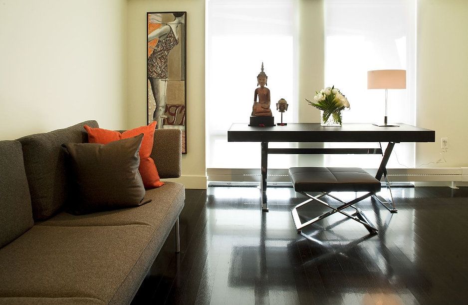 Modern office with a desk, bench, and a sofa. Features artwork, a lamp, and dark wood floor.