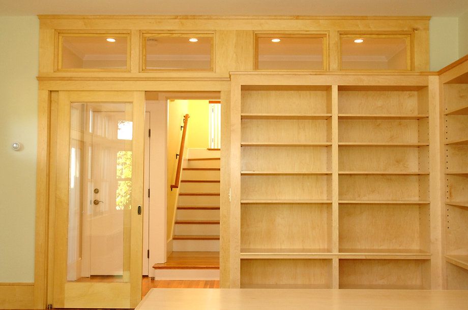Built-in wooden bookshelves and doorway with steps leading upward. Overhead, three lighted glass panels are visible.