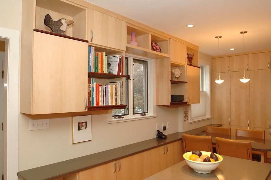Kitchen with light wood cabinets, open shelves with books, and a bowl of fruit.