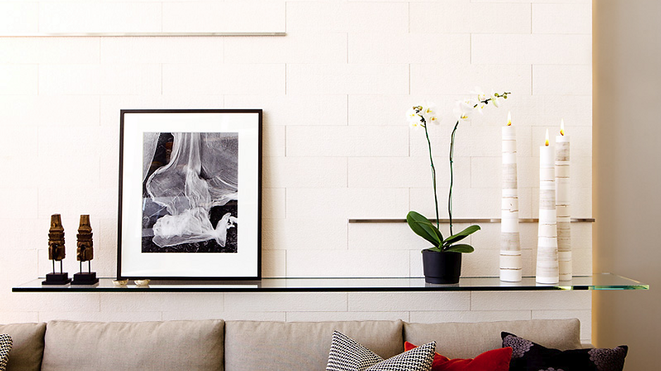 Shelf with art, potted orchid, and decorative candles above a sofa.
