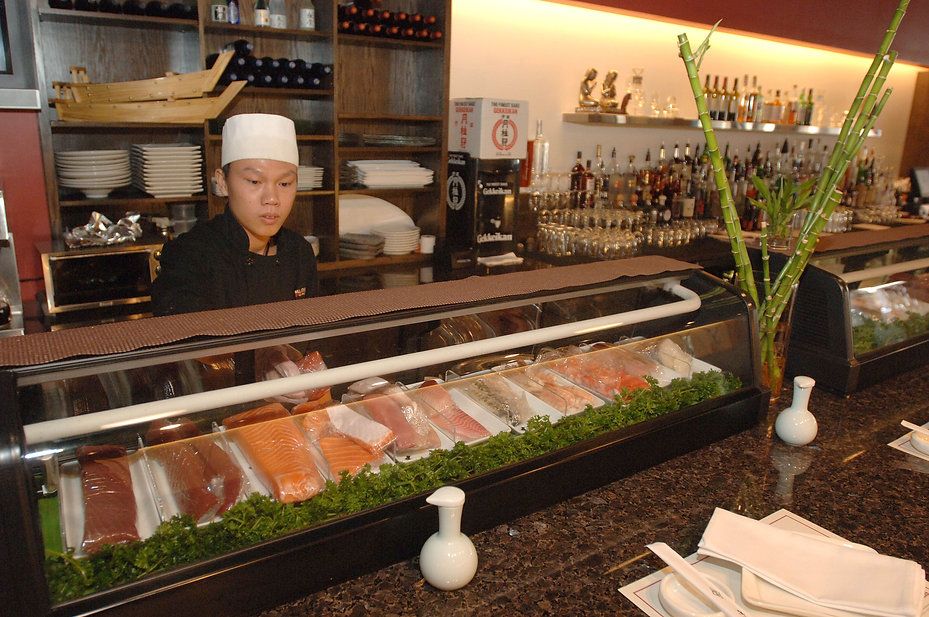 Sushi chef behind a glass display case filled with fish, in a restaurant setting.
