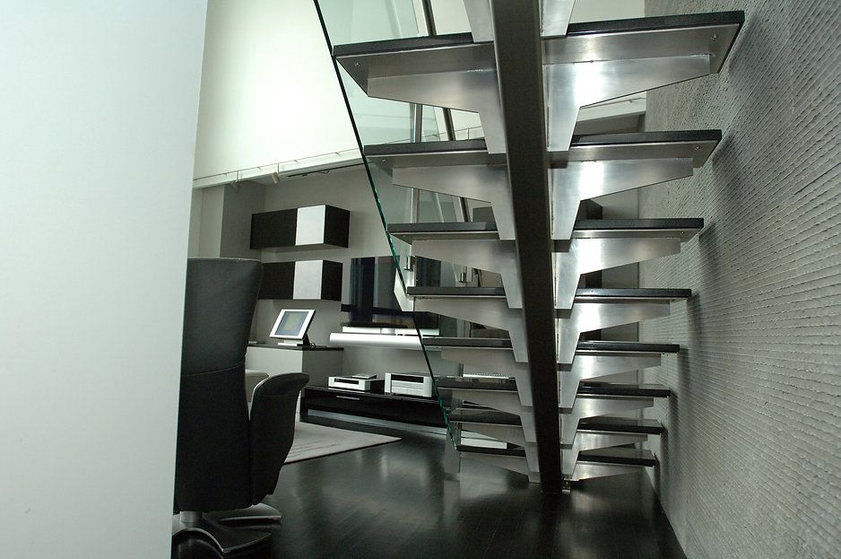 Modern staircase with glass railing, metal steps, dark flooring. Black and white decor in the background.