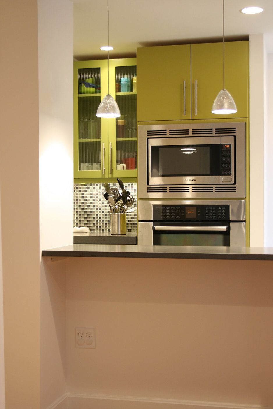 Built-in kitchen appliances in a brightly colored kitchen nook with hanging pendant lights.