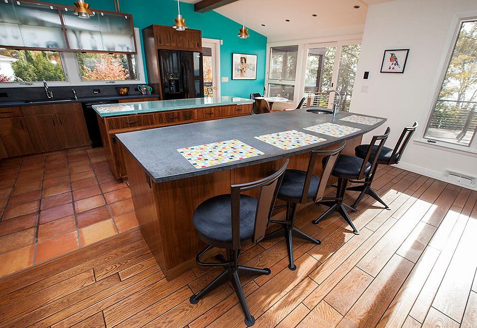 Kitchen with wood floors, a large island with stools, and a teal wall.