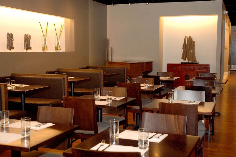 Empty restaurant interior with brown tables, chairs, booths; hardwood floor; neutral walls.