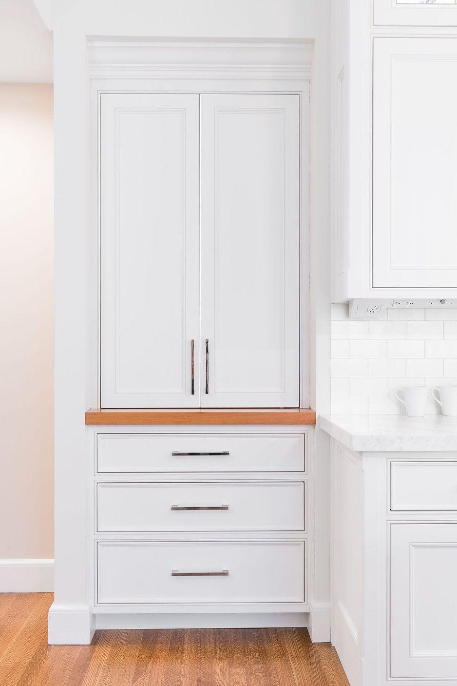 White kitchen cabinet with drawers and doors; wooden countertop.