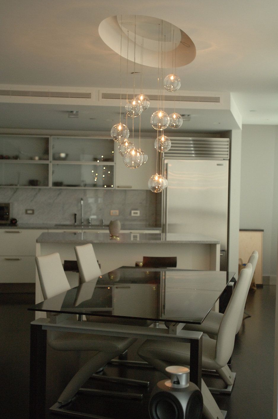 Modern kitchen with a dining table, overhead globe lights, and a large stainless steel refrigerator.