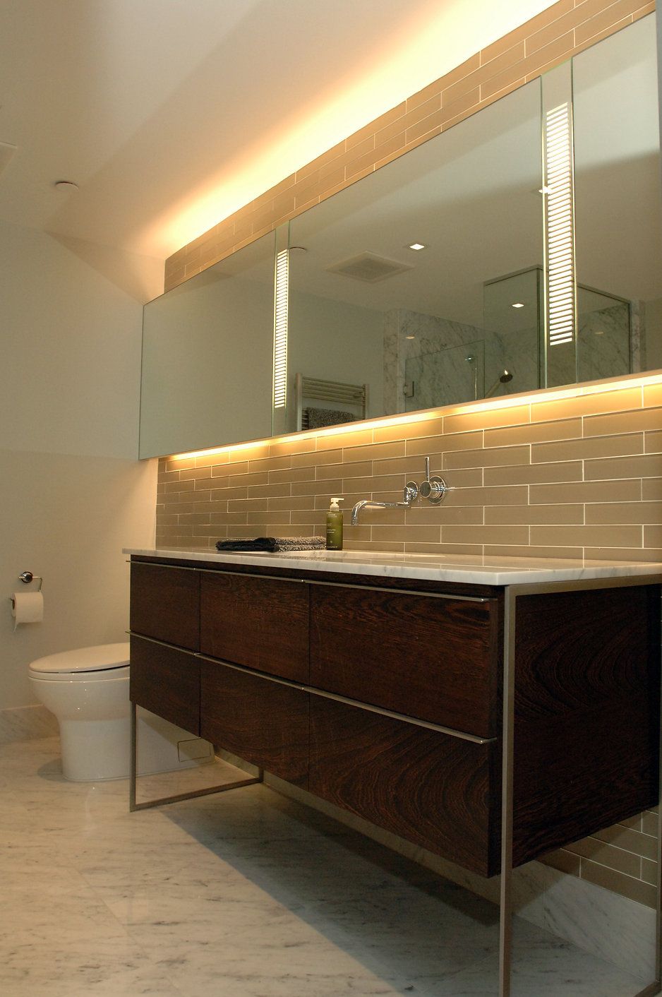 Modern bathroom with a dark wood vanity, large mirror, and under-mirror lighting.