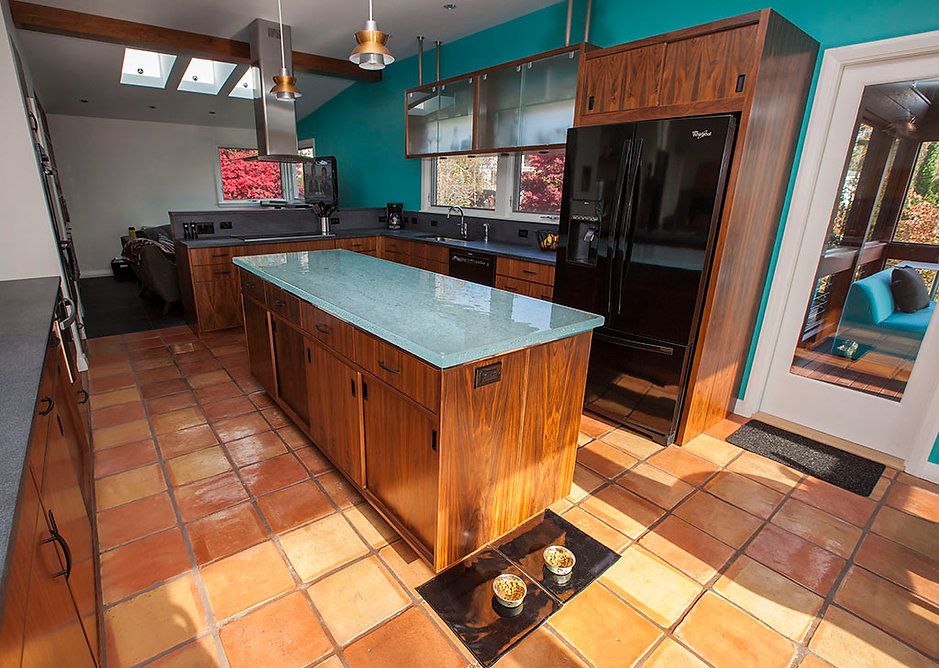 Modern kitchen with brown cabinets, turquoise wall, and terracotta tile floor.