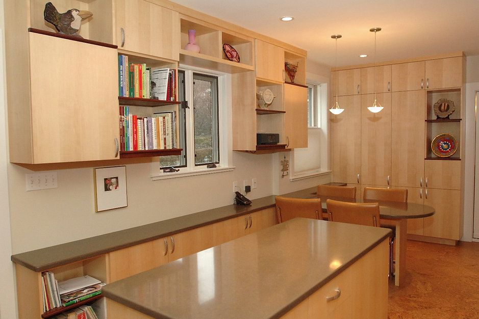 A modern kitchen with light wood cabinets, a gray countertop island, and a small dining table.