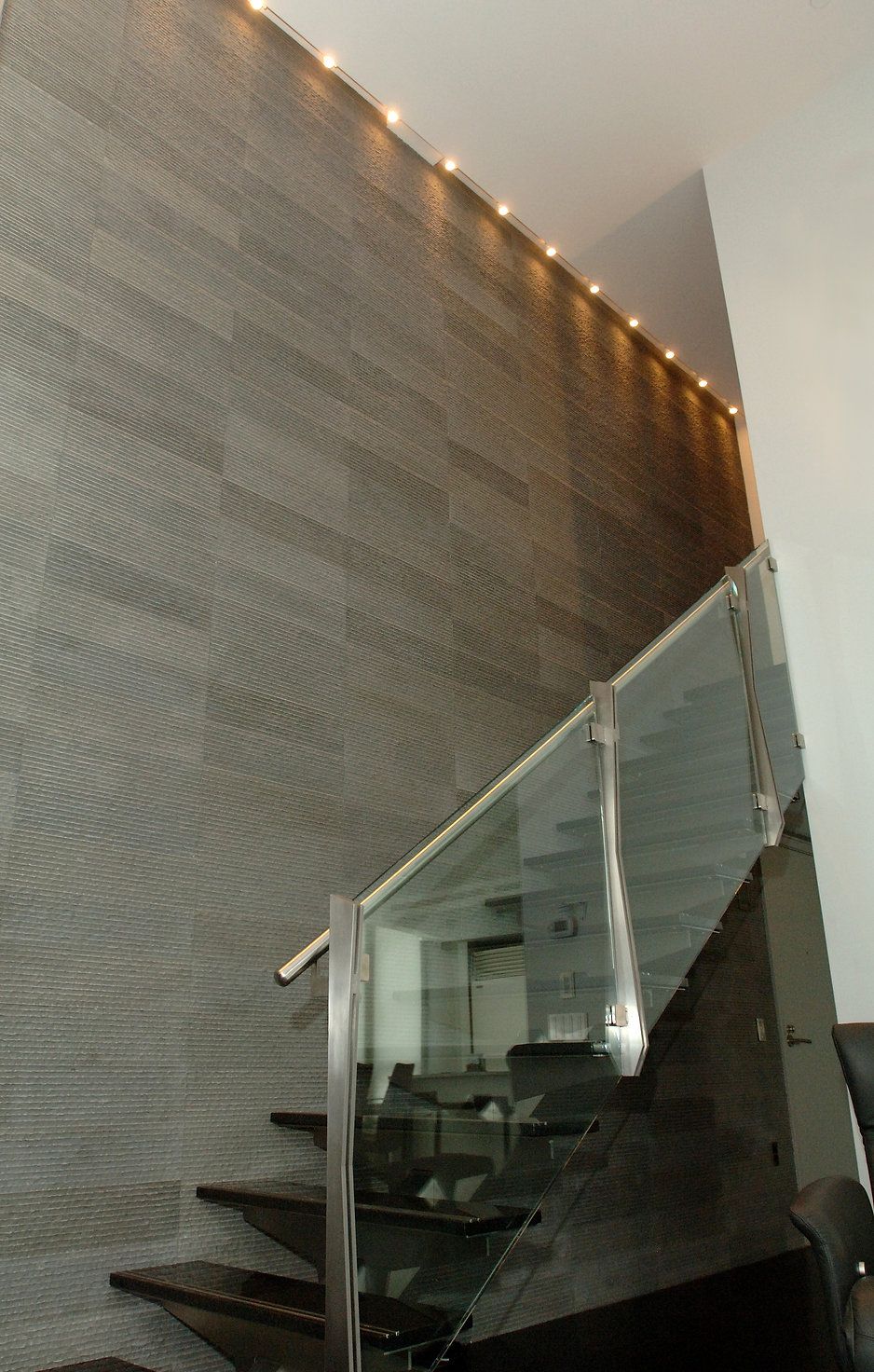 Staircase with glass railing and dark stone steps and wall, lit with small lights.