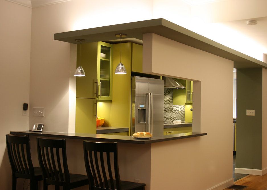 Bar-style seating area, dark chairs and countertop, with open view to a green kitchen.