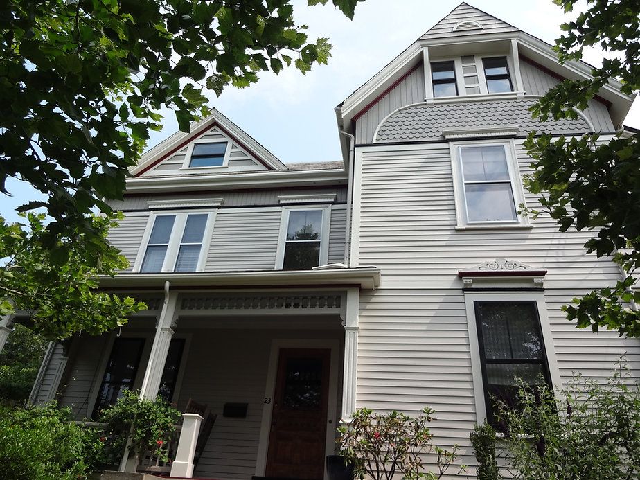 Two-story white house with porch, windows, and gabled roof, framed by tree branches against a cloudy sky.