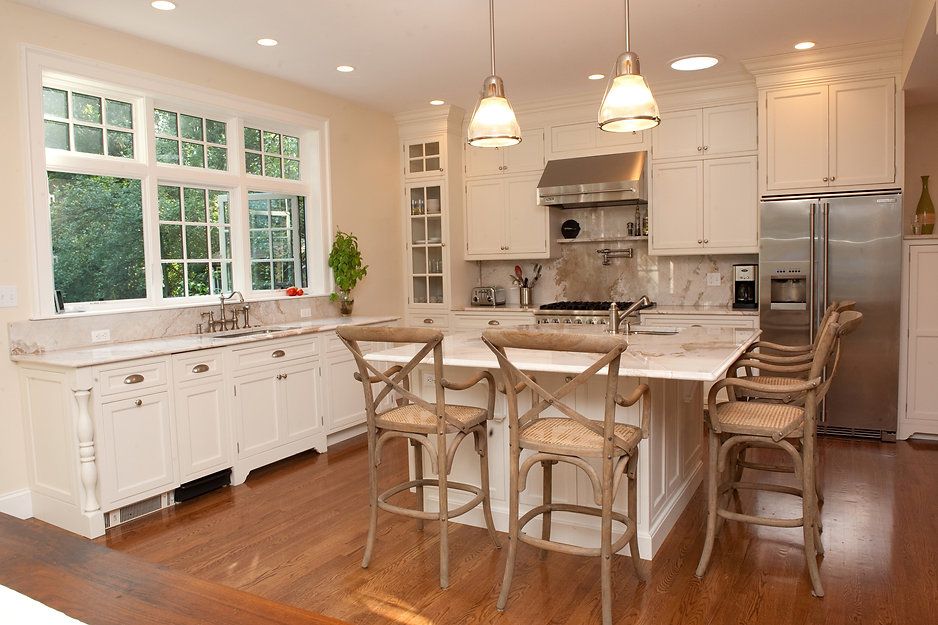 Spacious kitchen with white cabinets, island with bar stools, stainless steel appliances, and large windows.