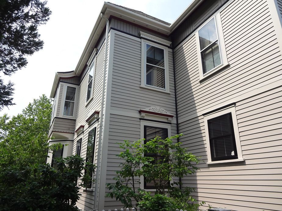 Multi-story light gray house with white trim and multiple windows.