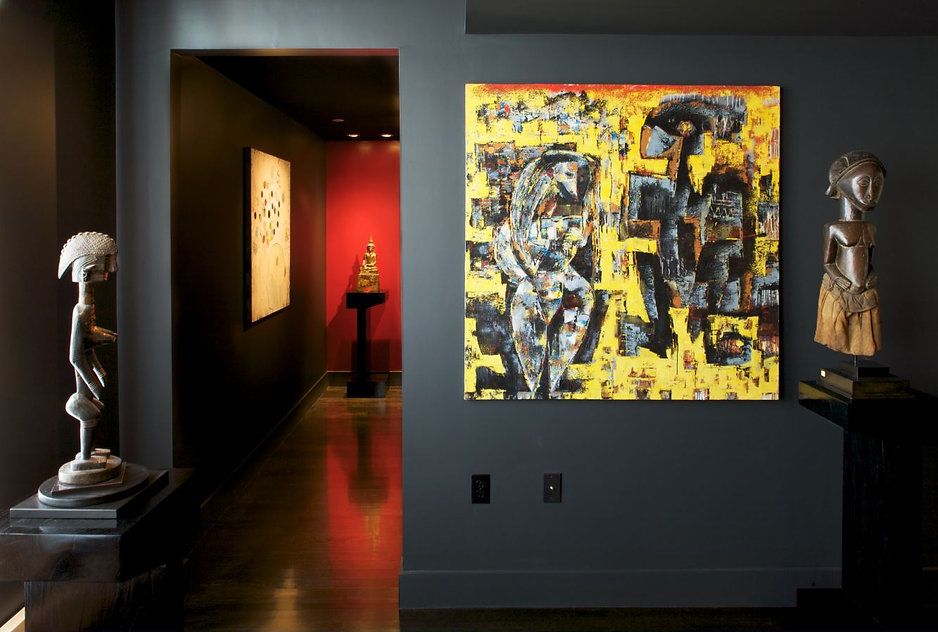 Dark hallway with art and sculptures on display, featuring a vibrant yellow and black abstract painting.