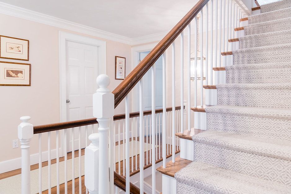 Staircase with white balusters, brown handrails, and light gray carpet. Soft pink walls with framed art and white doors.