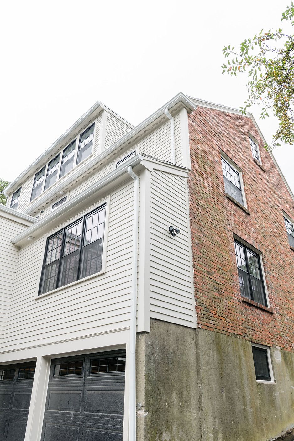 Two-story house, white siding and brick exterior, black garage doors. Cloudy sky.