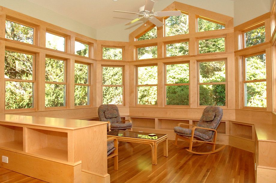 Sunroom with many windows, hardwood floors, and built-in seating. Two armchairs and a table are inside.