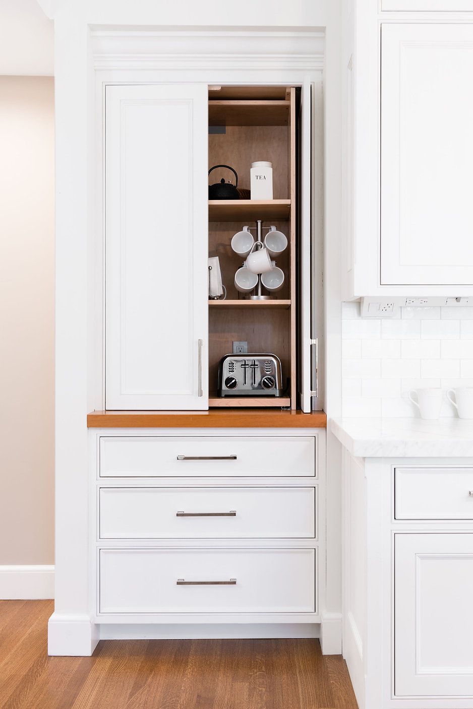 White kitchen cabinet with built-in coffee station: Toaster, mugs, shelves, drawers.