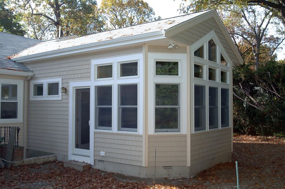 Sunroom addition on a house with white windows, beige siding, and a gable roof.