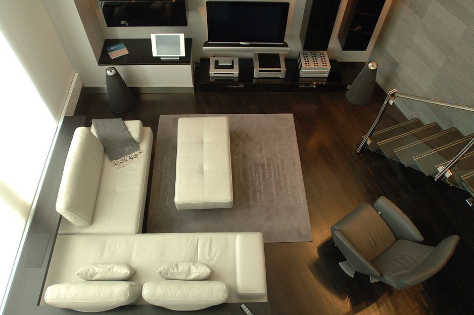 Modern living room with white sectional sofa, gray rug, black media console, and stairs.