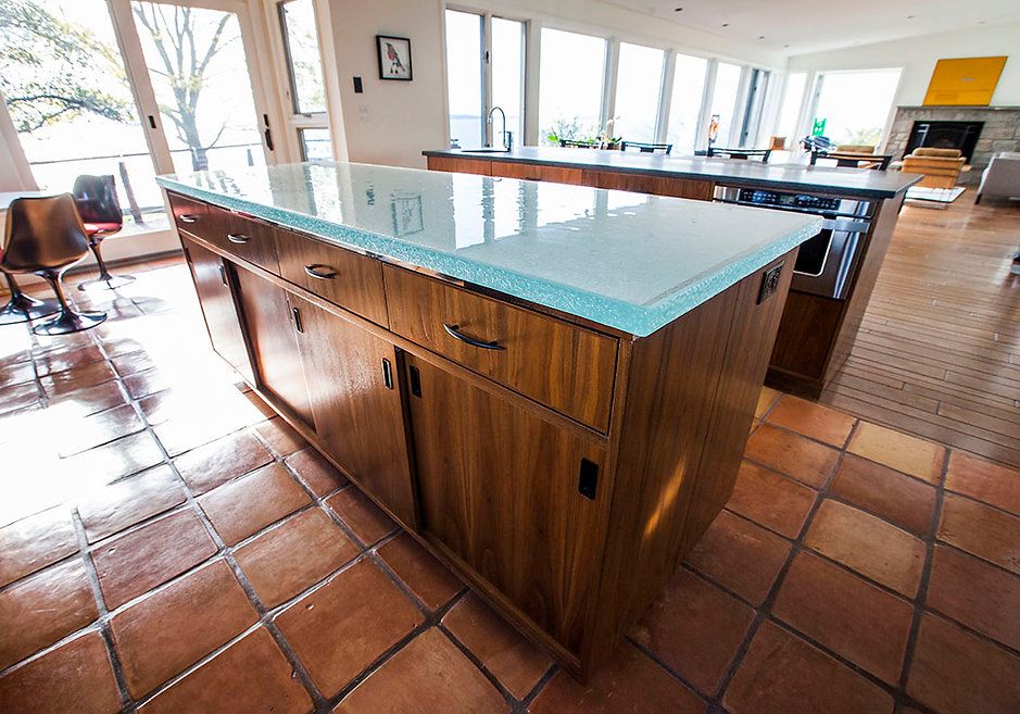 Wooden kitchen island with a light blue countertop, terracotta tile floor, and bright windows.