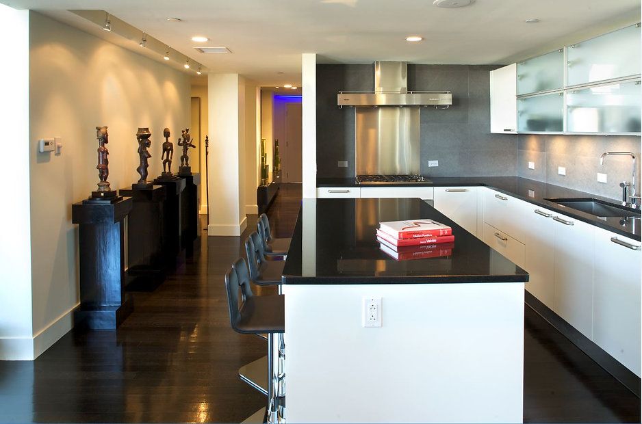 Modern kitchen with dark wood floors, white cabinets, black countertops, and stainless steel appliances.
