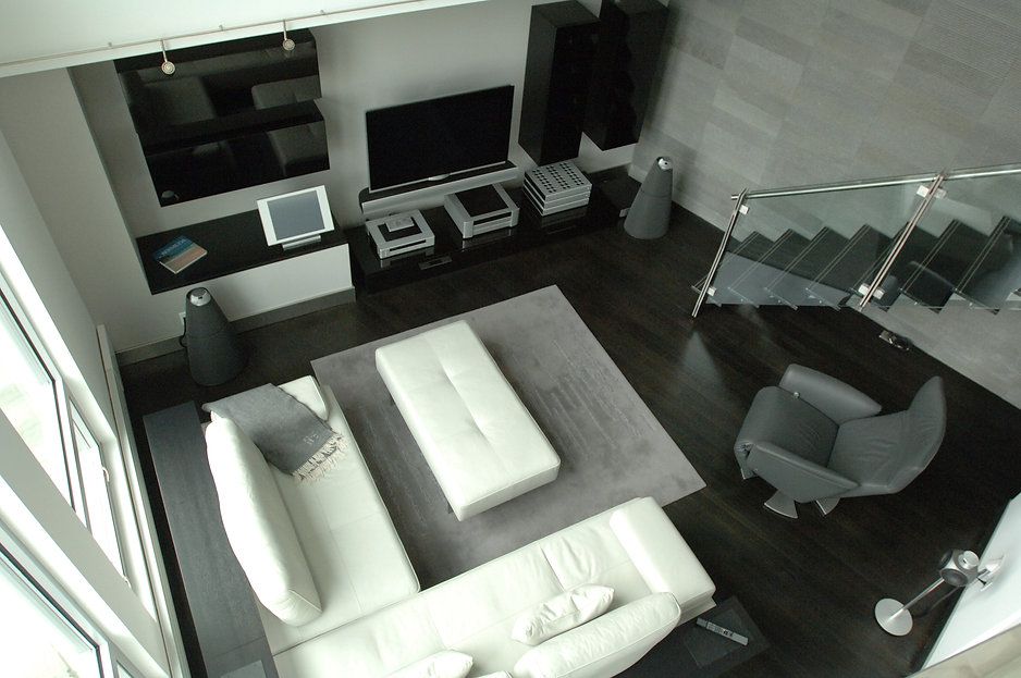 High-angle view of modern living room with white sofa, gray rug, stairs, and large TV. Dark wood floor, and gray walls.