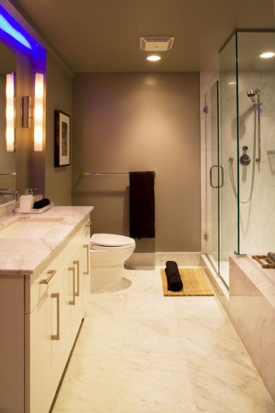Modern bathroom with white vanity, shower, toilet, and marble floors. Gray walls, brown towels, and a bamboo mat.