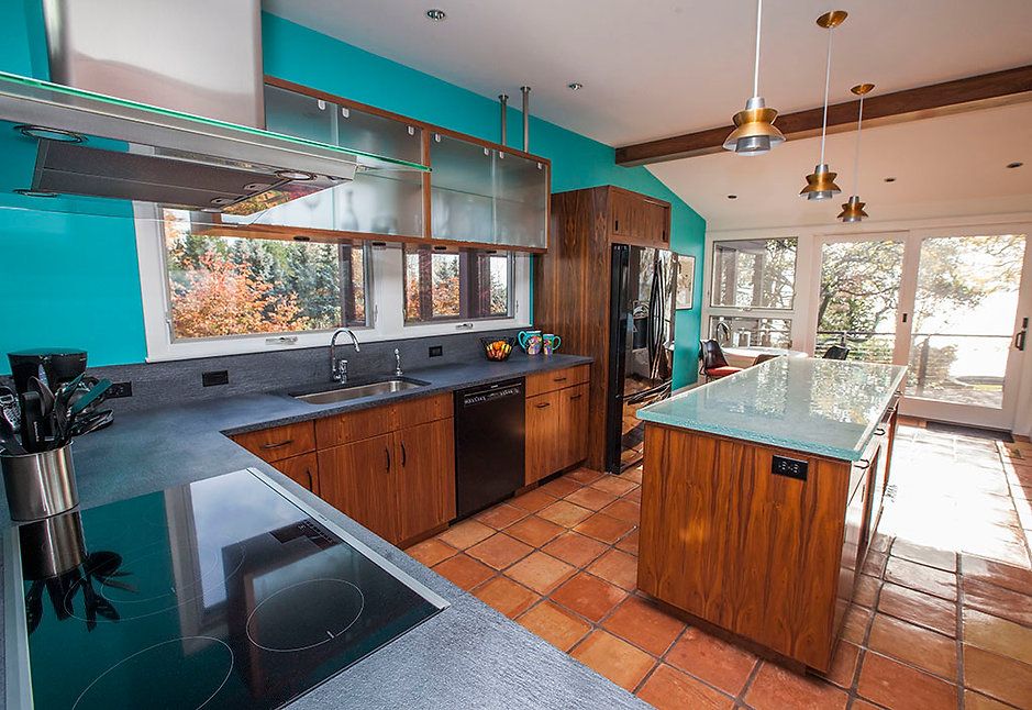 Bright kitchen with turquoise walls, wood cabinets, and a tiled floor. Island and a window.