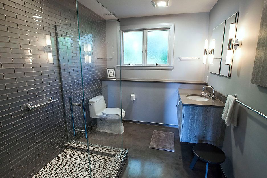 Modern bathroom with gray tile shower, toilet, sink, and a small window.