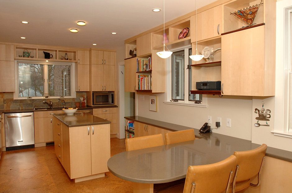 Modern kitchen with light wood cabinets, stainless steel appliances, and a gray countertop table with chairs.