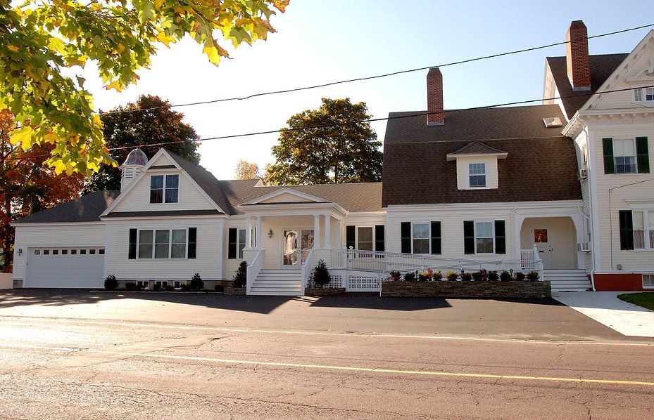 White house with black shutters, a porch, and a black paved driveway on a sunny day.