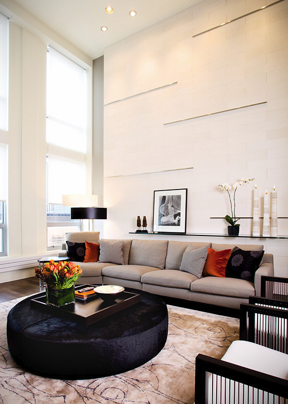 Living room with tall windows, neutral walls, a large gray sectional sofa, and a round black ottoman.