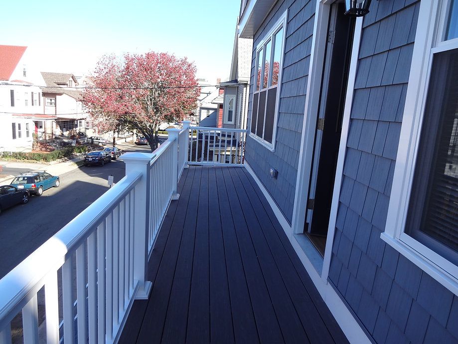 Deck with gray floorboards, white railing, blue siding, and a street view with trees.