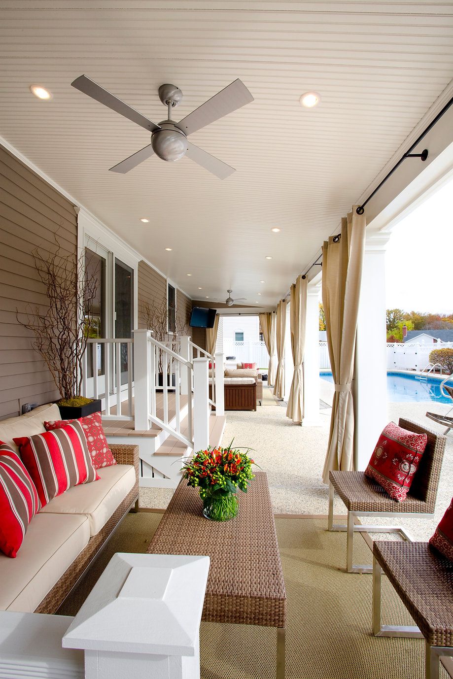 Covered outdoor patio with seating, red pillows, and a pool view.