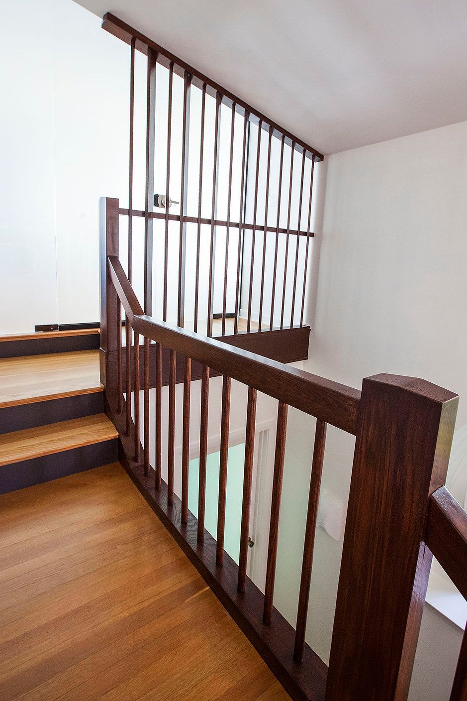 Wooden staircase with brown railings and vertical slats, leading upward.