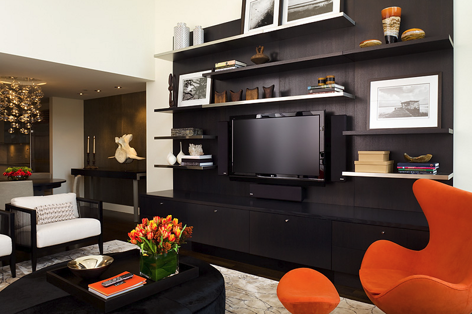 Modern living room with black shelving and media unit, orange accents, and white armchairs.