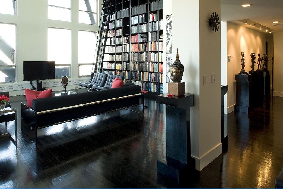 Modern living room with black furniture, tall bookshelves, and shiny dark wood floors.