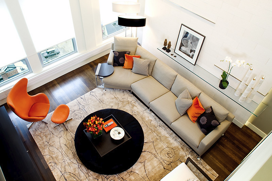 High-angle view of modern living room with orange chairs, beige sectional, black coffee table, and large windows.