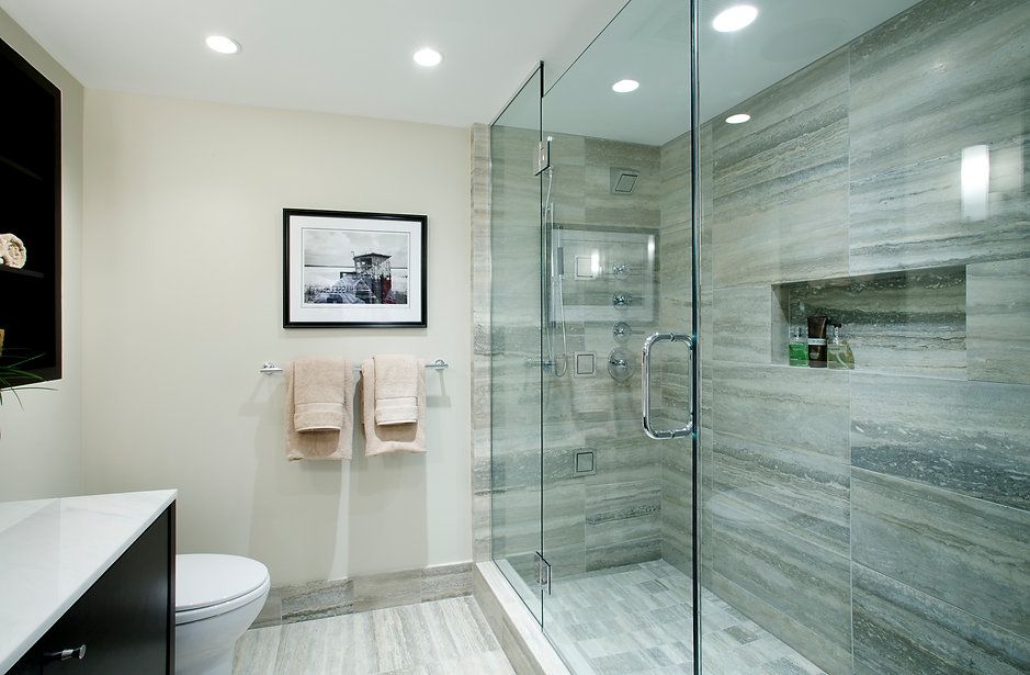 Modern bathroom with glass shower, gray tile walls, and a toilet.