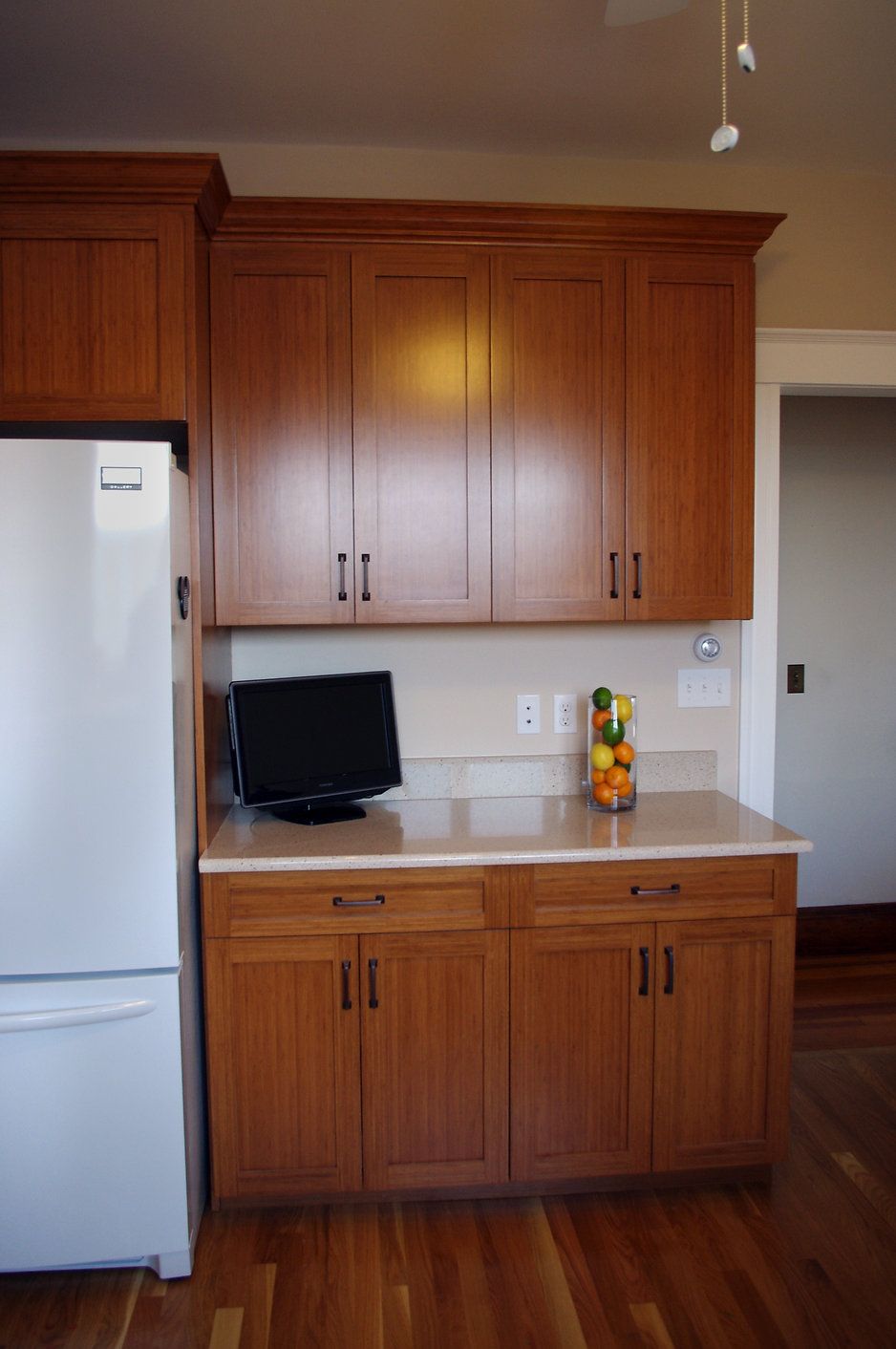 Kitchen with wooden cabinets, white refrigerator, counter with small TV, and fruit.